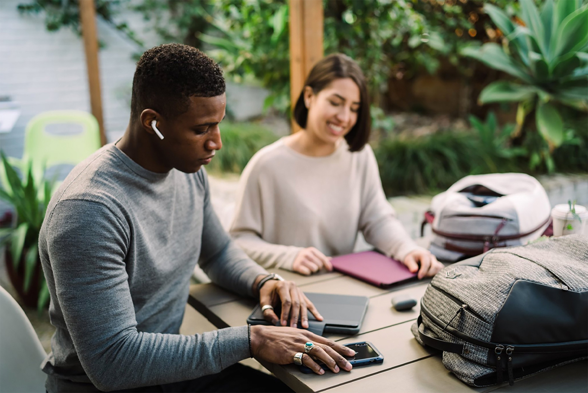 Two people, with devices and STM Goods backpacks, at an outdoor table