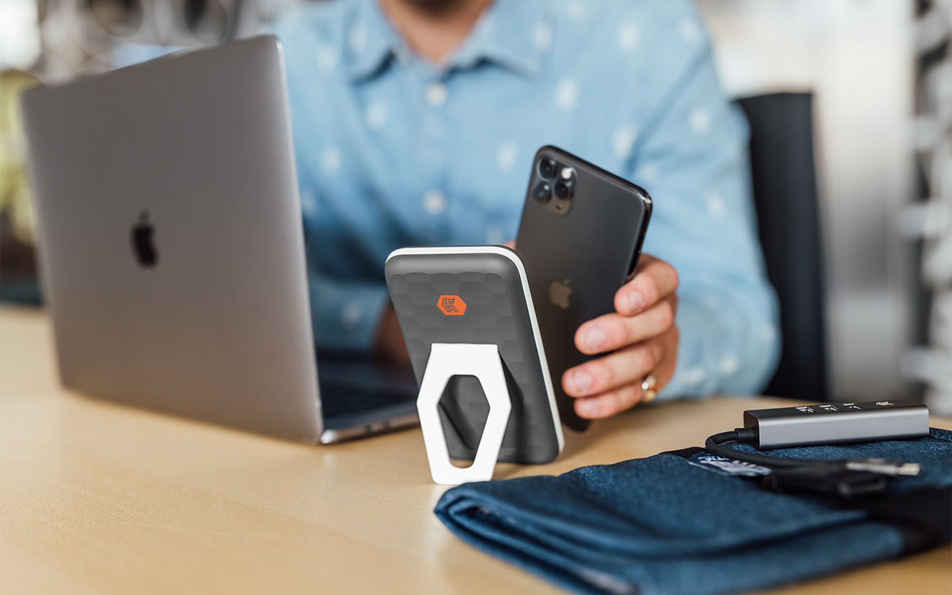 PowerKick, propped up on a desk next to an open laptop, with user about to connect an iPhone