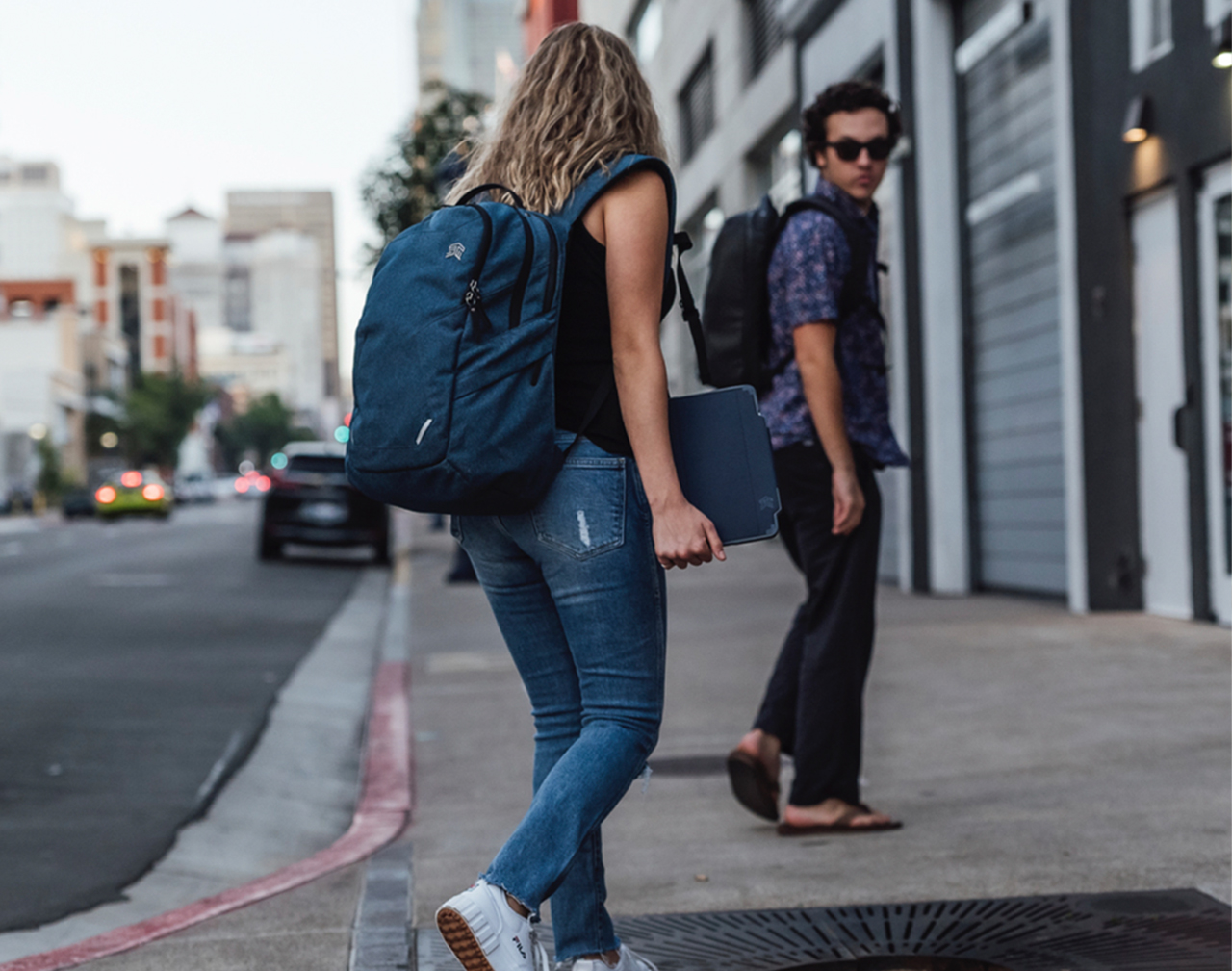 Two young people on street, with backpacks, one with laptop
